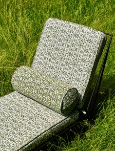 an outdoor chaise lounge in the middle of some tall grass with a roll of fabric covering it