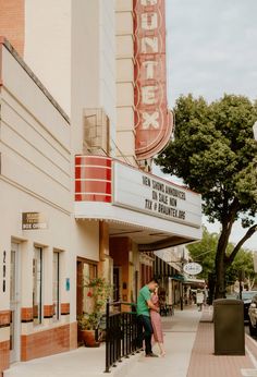 a man and woman kissing in front of a movie theater on the side of a street