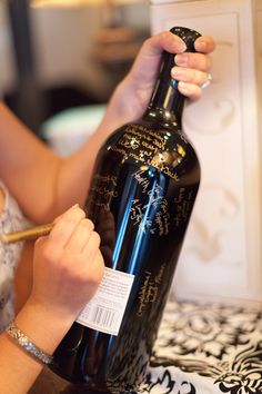 a woman is writing on a wine bottle