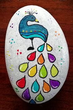 a painted rock with a peacock on it's face and drops of paint all over the surface