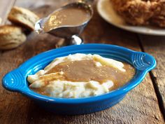 a blue bowl filled with mashed potatoes and gravy on top of a wooden table