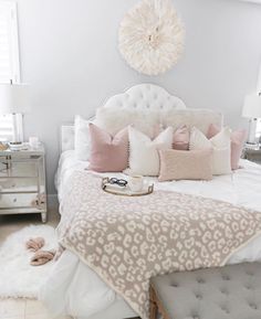 a white bed topped with lots of pillows next to a night stand and foot stool