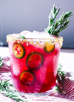 a red drink with cucumber and rosemary garnish on the rims