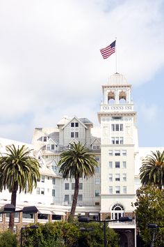 a large white building with a flag on top and palm trees in the foreground