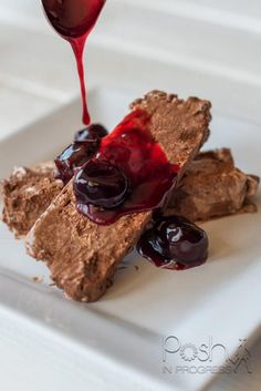 a piece of cake on a white plate with chocolate and cherries being drizzled over it