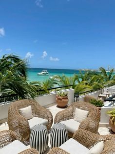 an outdoor seating area with wicker furniture and palm trees on the balcony overlooking the ocean