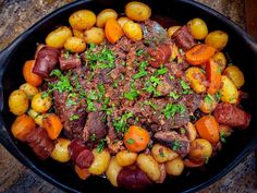 a skillet filled with meat, potatoes and carrots