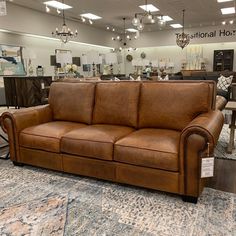 a brown leather couch sitting on top of a rug in a room filled with furniture