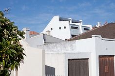 a white building with brown shutters and windows on the roof is next to a tree