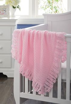 a crocheted pink blanket draped over a white crib