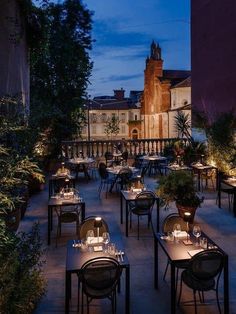 an outdoor dining area with tables, chairs and plants on the outside patio at night