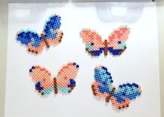 three cross stitch butterfly magnets sitting on top of a piece of white paper next to each other