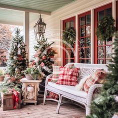 the porch is decorated for christmas with holiday trees and plaid pillows on white wicker furniture