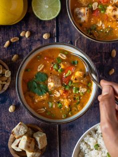 two bowls filled with soup and rice on top of a wooden table next to lemons