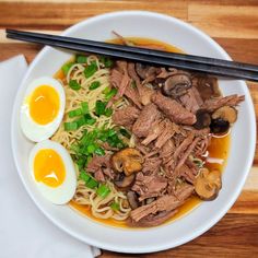 a white plate topped with meat and noodles next to chopsticks on top of a wooden table