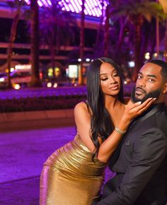 a man and woman posing for a photo in front of palm trees at night time