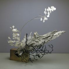 a piece of driftwood with white flowers and branches sticking out of it, against a gray background