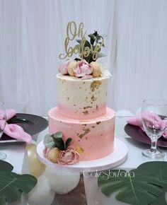 a three tiered cake with pink and gold frosting on top, surrounded by greenery