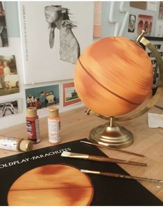 an orange globe sitting on top of a wooden table next to some paint and brushes