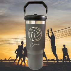 people playing volleyball on the beach at sunset with an equine logo tumbler cup