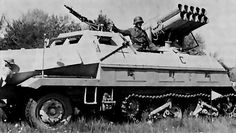 an armored vehicle with two men sitting on top of it's roof, in the middle of a field