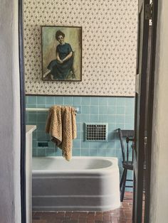 a painting hangs on the wall above a bathtub in a bathroom with tile flooring