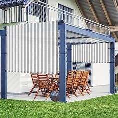 an outdoor dining area with wooden chairs and table under a metal structure on the grass