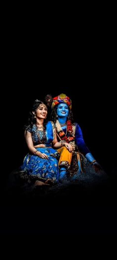 two women are sitting on the ground with their arms around each other, both dressed in blue and yellow