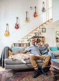 a man and woman sitting on a couch with a dog in front of the stairs