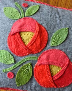 a close up of a pillow on a wooden table with an embroidered apple and leaf design