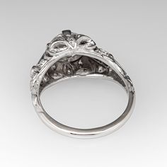 This gorgeous circa 1930s Art Deco engagement ring features a pierced and engraved design and milgrain details. The ring is centered with a 1.30 carat round transitional brilliant cut diamond, in a four-prong setting. The diamond is GIA certified M color and VS1 clarity. The top of the ring is bead set with 16 round single cut diamonds. The shoulders are each channel set with two square step cut lab created sapphires. The ring measures 9.9mm at the top and rises 7.6mm above the finger. The ring is currently a size 6 and we offer complimentary resizing to fit. The ring is platinum and the shank was replaced some time ago with sturdy 14k white gold and looks great. Victorian Diamond Ring With Round Cut, Antique Platinum Cluster Ring, Antique Platinum Diamond Ring With Center Stone, Vintage Platinum Round Ring, Classic Engraved Ring With Brilliant Round Cut, Classic Engraved Ring With Brilliant Cut Round Band, Antique Platinum Cluster Ring With Center Stone, Classic Engraved Ring With Brilliant Cut, Timeless Engraved Ring With Brilliant Cut