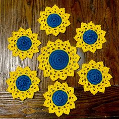 six crocheted yellow and blue flowers sitting on top of a wooden table