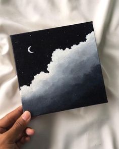 a hand holding up a black and white painting with the moon in the sky above it