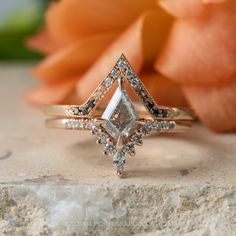 a diamond ring sitting on top of a stone slab next to an orange flower with petals in the background