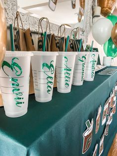 there are many cups on the table with green and white decorations around them, along with balloons