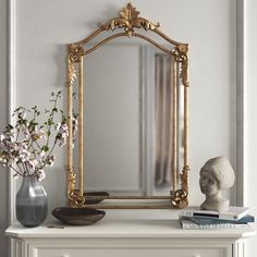 a white dresser topped with a mirror next to a vase filled with flowers and books