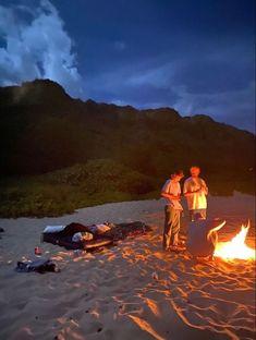 two men standing next to a fire on the beach