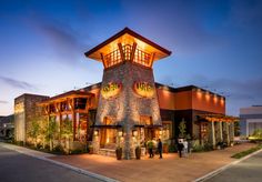 the front of a restaurant with people standing outside at night, lit up by lights