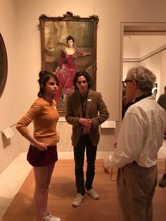 two men and a woman standing in front of a painting on display at an art museum