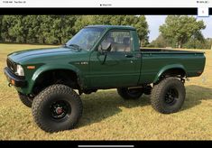 a green pick up truck parked on top of a grass covered field