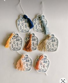 four ceramic tags with tassels on them sitting on a white table top next to each other