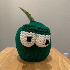 a knitted green beanie with two eyes on top of a wooden table in front of a white wall