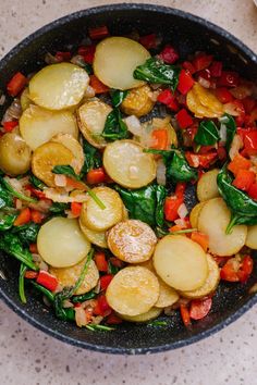 a pan filled with potatoes and spinach on top of a marble countertop next to utensils