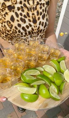 a person holding a tray filled with glasses and limes