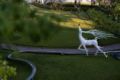 two white sculptures in the shape of horses on a wooden walkway surrounded by green grass