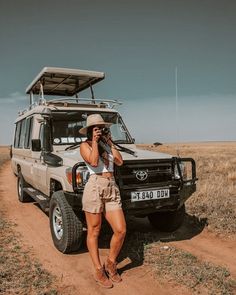 a woman standing in front of a vehicle on a dirt road