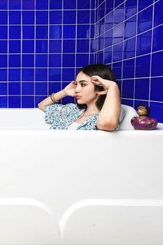 a woman sitting in a bathtub with her hand on her head and looking off to the side