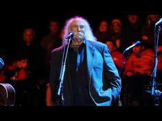 an older man singing into a microphone in front of a group of people on stage