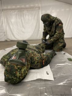 two soldiers in camouflage gear laying on the ground next to each other and one is holding a water bottle