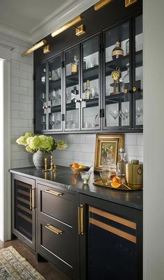 a kitchen with black cabinets and gold trim on the countertop, along with a vase filled with flowers